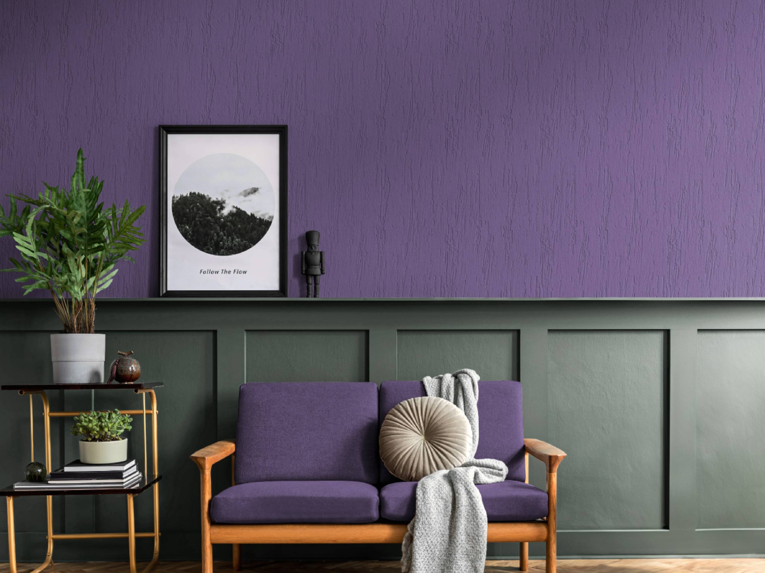 Sala moderna con pared revestida en textura violeta y boiserie verde oscuro, sofá de madera con tapizado púrpura y decoración minimalista.